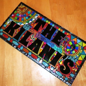 May include: A rectangular mosaic art piece with the words "KIL THE KLANS" in large black letters. The mosaic features a colorful array of glass tiles in various shapes and sizes, including red, blue, green, and yellow.