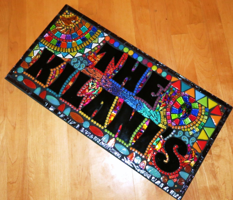 May include: A rectangular mosaic art piece with the words "KIL THE KLANS" in large black letters. The mosaic features a colorful array of glass tiles in various shapes and sizes, including red, blue, green, and yellow.