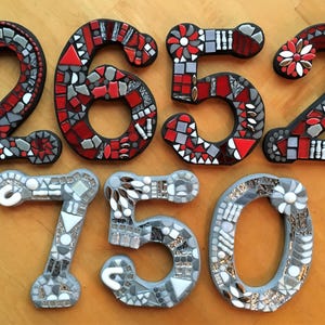 three mosaic numbers, each composed of small tiles in various colors and patterns, arranged on a wooden surface.