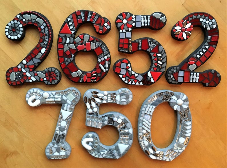 three mosaic numbers, each composed of small tiles in various colors and patterns, arranged on a wooden surface.