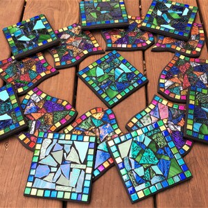 K&ouml;nnte beinhalten: Eine Sammlung von 13 bunten Mosaik-Untersetzern mit verschiedenen geometrischen Mustern. Die Untersetzer bestehen aus kleinen Glassplittern und haben einen schwarzen Rand.