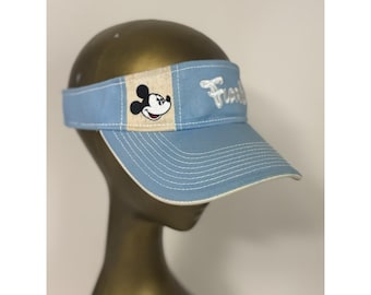 Könnte beinhalten: Hellblaue Sonnenblende mit gebogenem Schirm und weißen Nähten. Die Sonnenblende hat ein beiges Feld mit einer Mickey Mouse-Grafik und dem Wort "Fun" in Weiß gestickt. Die Sonnenblende wird auf einem Schaufensterkopf präsentiert.