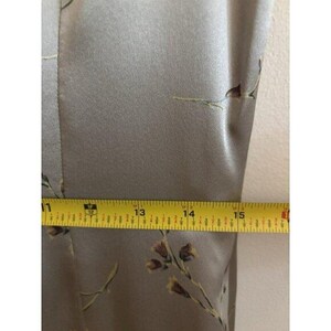 May include: Close-up of a light olive green fabric with a floral pattern. A yellow measuring tape shows a measurement of approximately 33 to 38 cm. The fabric has a subtle sheen.