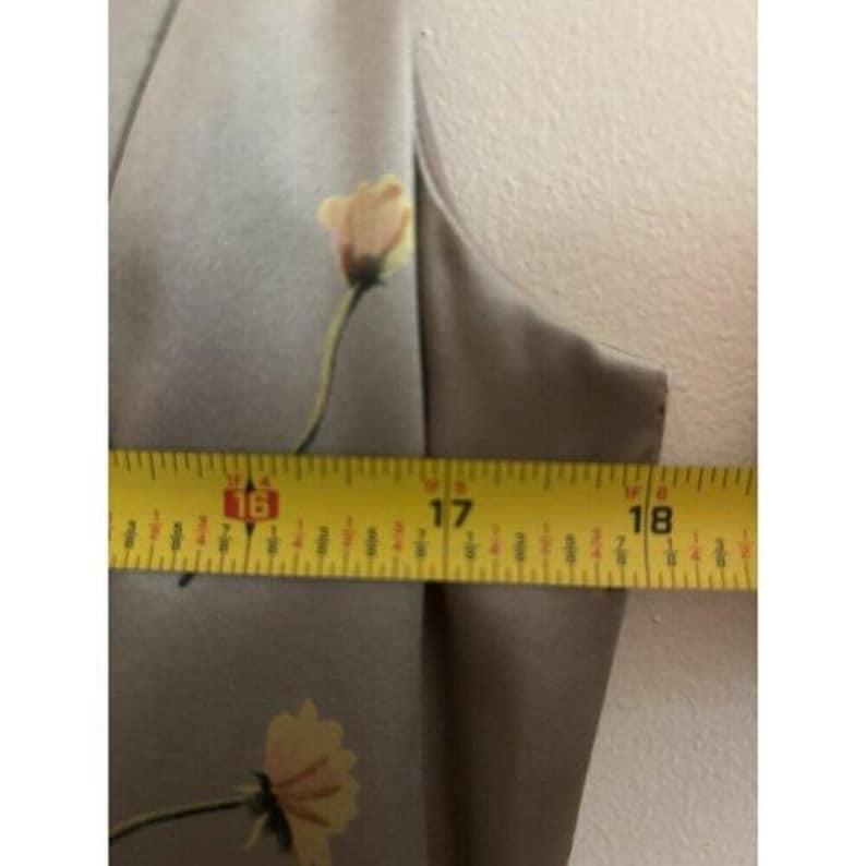 May include: A close-up of a light brown dress with a floral pattern. The dress is measured with a yellow tape measure, showing a measurement of approximately 40.6 to 45.7 cm.