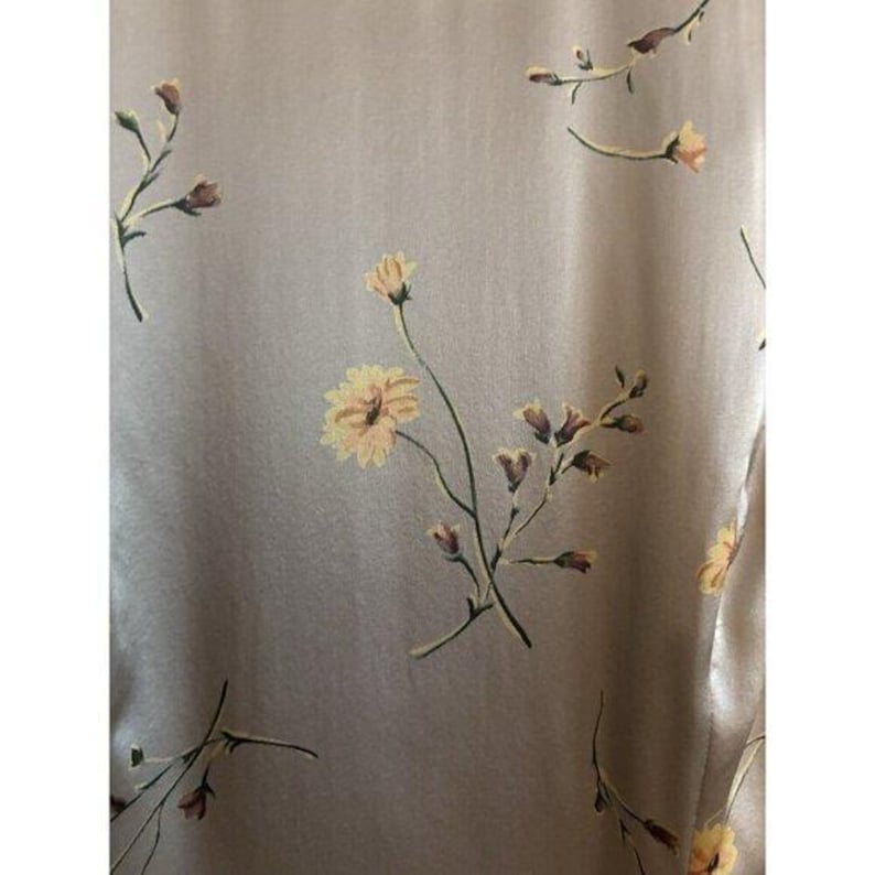 May include: A close-up of a fabric with a floral design. The fabric is a pale beige with a slight sheen. The surface is adorned with delicate yellow and brown flowers and buds, creating a soft, natural pattern. The floral design adds a touch of elegance to the fabric.