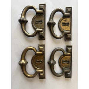 May include: Set of four antique brass cabinet door pulls with a keyhole design. Each pull has a decorative, ornate design with a rounded top and a keyhole in the center.