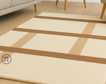 May include: Cream-colored rectangular rug with a geometric pattern of brown and tan stripes. The rug is placed on a light wood floor, and the design features a series of horizontal and vertical lines.