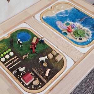 Peut inclure: Deux plateaux en bois avec des scènes de ferme et d'océan. La scène de la ferme comprend un tracteur rouge, des animaux et des cultures. La scène océanique présente une île miniature avec du corail et un dauphin. Les deux scènes sont dans un cadre en bois.