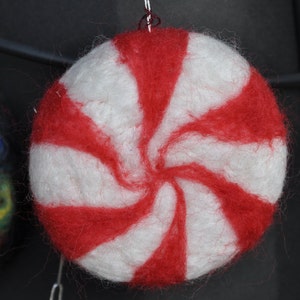 May include: A white and red peppermint candy ornament made of felt. The ornament is shaped like a peppermint candy and has a red and white swirl pattern.