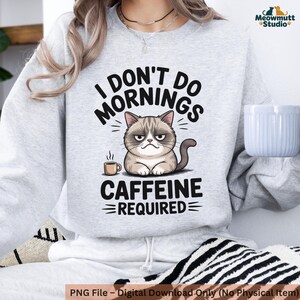 May include: A light gray sweatshirt with the text "I DON'T DO MORNINGS CAFFEINE REQUIRED" and a cartoon image of a grumpy cat with a coffee cup. The sweatshirt is a digital download.