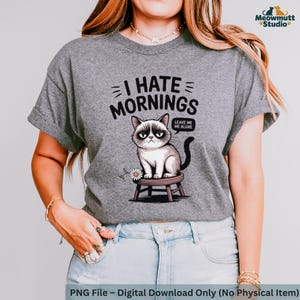 May include: Gray t-shirt with the phrase "I HATE MORNINGS" and a grumpy cat illustration. The cat is sitting on a small stool with a daisy. The text "LEAVE ME ALONE" is in a speech bubble.