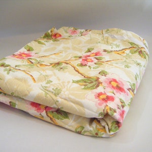 May include: A folded fabric with a floral pattern in shades of pink, yellow, and green. The fabric has a white background with a subtle texture.