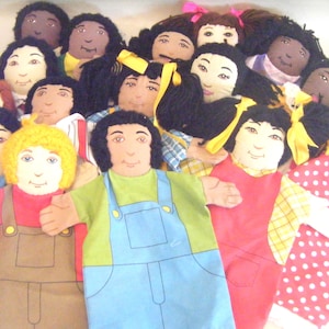 May include: A group of 14 colorful hand puppets with different facial features and hairstyles. The puppets are made of fabric and have a variety of clothing styles, including overalls, dresses, and shirts.