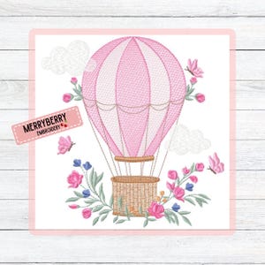 Pode incluir: Design bordado com um balão de ar quente rosa e branco com uma cesta tecida, rodeado por flores rosa e azuis, borboletas e nuvens. O texto "MERRYBERRY EMBROIDERY" está em uma etiqueta rosa.