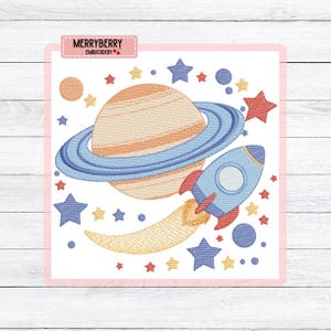 May include: Embroidered space-themed design featuring a planet with rings, a blue rocket, and stars in shades of blue, orange, and red. The design includes the text "MERRYBERRY EMBROIDERY" in a pink rectangle.