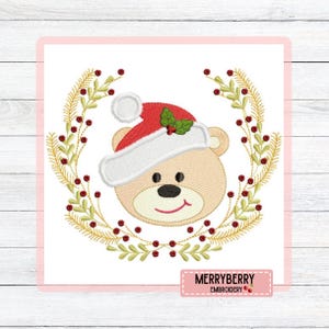 Pode incluir: Design bordado de um ursinho de pelúcia usando um gorro de Papai Noel, cercado por uma coroa de folhas douradas e bagas vermelhas. O urso tem um rosto sorridente. O texto "MERRYBERRY EMBROIDERY" está na parte inferior.