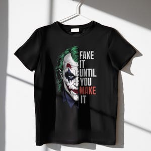 May include: Black t-shirt featuring a graphic of the Joker's face with green hair, white face paint, and red lipstick. The text "FAKE IT UNTIL YOU MAKE IT" is printed vertically on the right side of the image.
