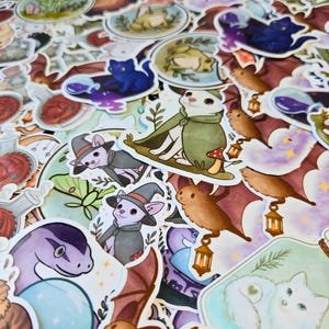 Puede incluir: Una colecci&oacute;n de pegatinas coloridas con ilustraciones caprichosas. Los dise&ntilde;os incluyen un gato blanco con una capa verde, un gato azul, una serpiente morada, murci&eacute;lagos y botellas de pociones. Tema de fantas&iacute;a.