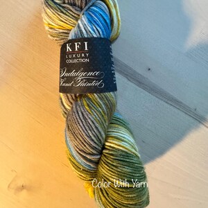 May include: A skein of hand-painted yarn in shades of blue, yellow, green, and gray. The yarn is labeled "KFI Luxury Collection Indulgence Hand Painted." The words "Color With Yarn" are printed on the bottom of the image.