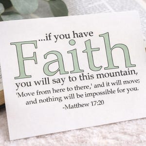 May include: A white card with the word "Faith" in green script, along with a quote from Matthew 17:20. A beige mug filled with coffee sits to the right of the card, next to an open book. Green leaves are in the background.