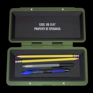 May include: An olive green rectangular storage case with a black interior lining. The lid features the white text CASE: DB-S147 PROPERTY OF SPERANZA. Inside, two yellow pencils, a clear plastic pen, and a blue and black ballpoint pen are stored.