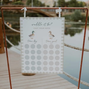 May include: A gender reveal voting board with the text "Waddle it be? Cast your vote!" features watercolor duck illustrations. The board is divided into "Team Boy" and "Team Girl" sections with voting circles. The sign is framed by a copper-colored metal stand.
