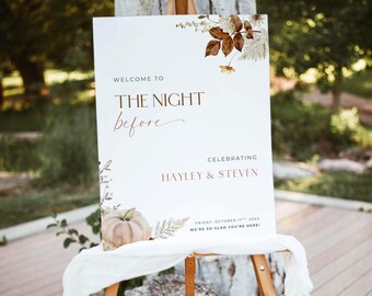 May include: A white rectangular wedding welcome sign on a wooden easel featuring brown text that reads: WELCOME TO THE NIGHT before CELEBRATING HAYLEY & STEVEN FRIDAY, OCTOBER 17TH, 20XX WE'RE SO GLAD YOU'RE HERE! Decorated with brown autumn leaves and a pumpkin.