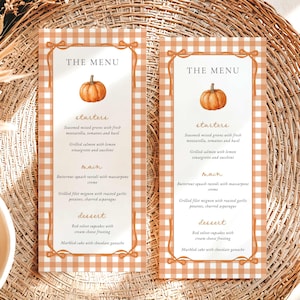 May include: Two vertical menu cards featuring an orange and white gingham border with a pumpkin illustration at the top. The text reads THE MENU, starters, main, and dessert, listing items like seasoned mixed greens, salmon, ravioli, and cupcakes.