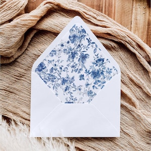 May include: A white envelope with an open triangular flap featuring an interior liner decorated with a blue and white floral pattern. The design consists of detailed botanical illustrations of various flowers and leaves in shades of blue.