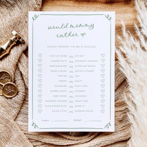 May include: A white rectangular game card titled would mommy rather with sage green text and a matching border. The card lists choices like stay at home or go out, diaper duty or midnight feeding, and includes heart icons for checking answers.