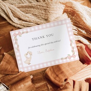 May include: A rectangular thank you card featuring a light pink and white gingham border. The text reads THANK YOU, for celebrating this special day with us!, and Love, Sophia. A small illustration of two ducks and pink ribbons decorates the card.