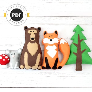Puede incluir: Un conjunto de juguetes de animales del bosque de fieltro, que incluye un oso marrón, un zorro naranja, un ratón gris y un árbol de Navidad verde. Los juguetes están dispuestos en fila sobre un fondo de madera blanca. El texto "HAND SEWING PDF PATTERN" es visible en un círculo amarillo.