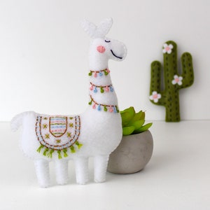 Felt llama leaning on a plant with felt cacti in the background