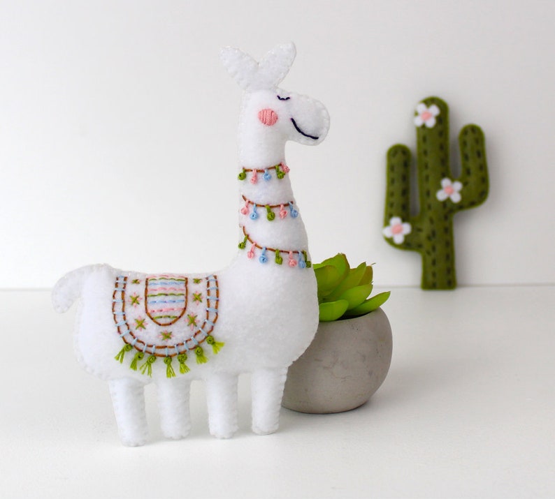 Felt llama leaning on a plant with felt cacti in the background