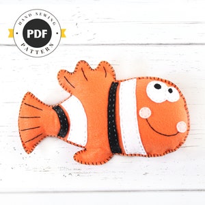 May include: A felt orange and white clownfish with black stripes and a smiling face. The fish is a hand-sewn PDF pattern.