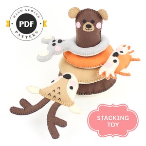 Puede incluir: Un juguete de apilar de fieltro con un oso marrón, un ratón gris, un ciervo marrón y un zorro naranja. El juguete está etiquetado como "Stacking Toy".
