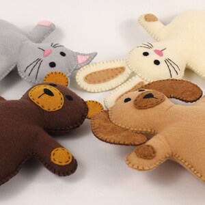 Four hand sewn stuffed animals lying on their backs with heads together: cat, rabbit, dog, and bear