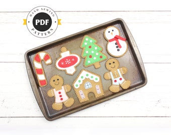 May include: A set of felt Christmas ornaments on a baking sheet. The ornaments include a gingerbread man, a gingerbread house, a candy cane, a Christmas tree, an ornament, and a snowman.