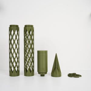 Puede incluir: Objetos impresos en 3D de color verde oliva, que incluyen dos cilindros altos con patrones de celosía, un cilindro más corto con el texto "moss buddy", un objeto en forma de cono y varios anillos pequeños. Los objetos están dispuestos sobre una superficie blanca.