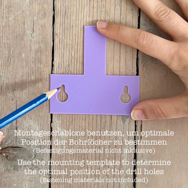 May include: A purple mounting template with two keyhole-shaped cutouts, used to determine the optimal position for drill holes. A blue pencil is positioned to mark a hole. The template is placed on a wooden surface.