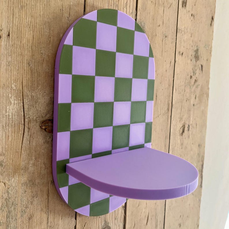 May include: A purple and green checkered wall shelf with a rounded top and a small shelf. The shelf is mounted on a wooden surface. The shelf is approximately 10 inches wide and 6 inches deep.