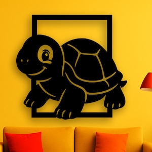 Pode incluir: Uma obra de arte de parede de tartaruga preta com contorno dourado, definida dentro de uma moldura quadrada preta. A tartaruga está sorrindo. A arte é exibida em uma parede amarela acima de um sofá amarelo com almofadas vermelhas e laranja. Um tapete e uma lâmpada vermelhos também são visíveis.