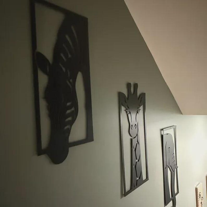 May include: Black metal wall art featuring a zebra, giraffe, and elephant. Each animal is depicted in a framed silhouette. The artwork is mounted on a light green wall, creating a decorative display.