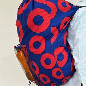 May include: A blue drawstring backpack with a red donut pattern. The backpack has a mesh side pocket and is being worn by a person.