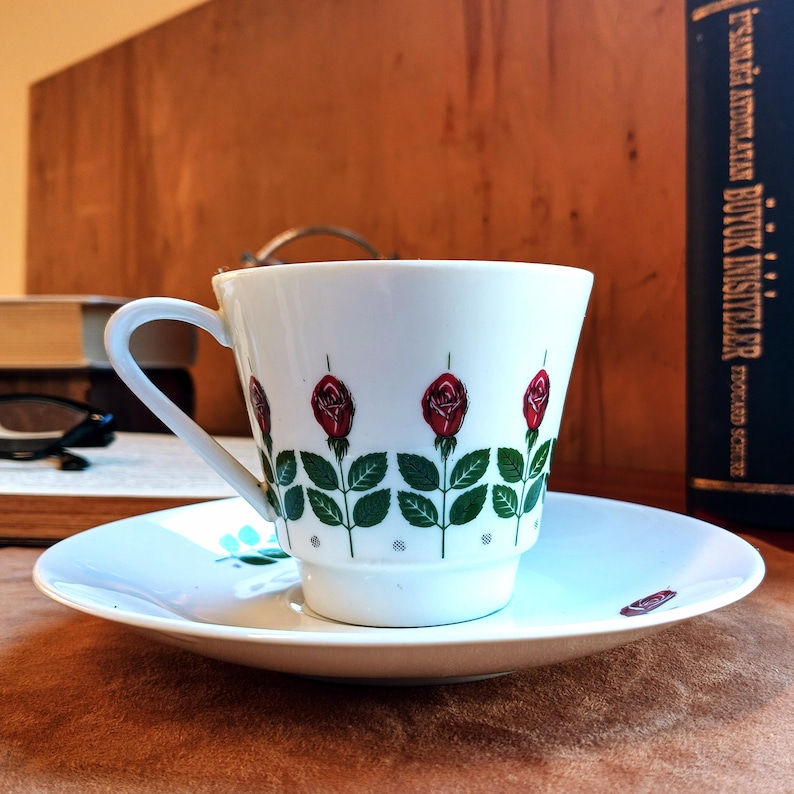 Pu&ograve; includere: Servizio da t&egrave; bianco con motivo floreale a rose. La tazza presenta un manico curvo e un motivo ripetuto di rose rosse con foglie verdi. Il piattino ha un design abbinato e un piccolo accento floreale.