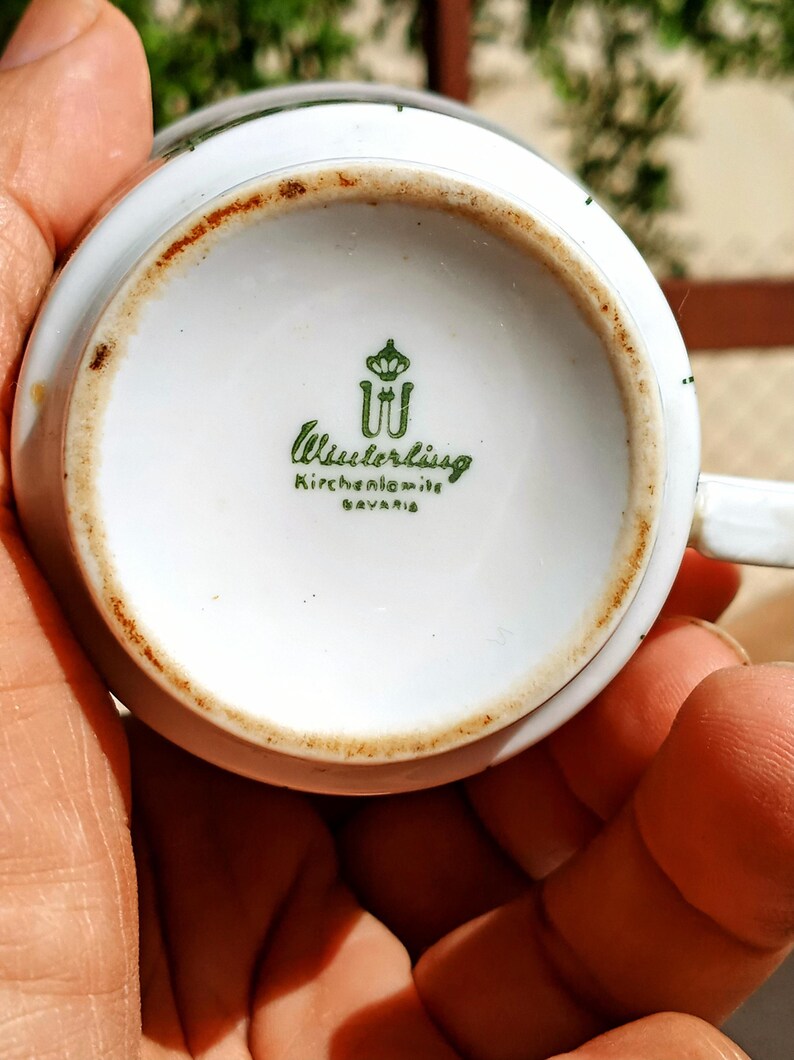 Pu&ograve; includere: Base di una tazza da t&egrave; in porcellana bianca con logo verde e scritta "Wieslerlissg Kirchenlamitz BAYERN". La tazza ha un bordo marrone e un piccolo manico.