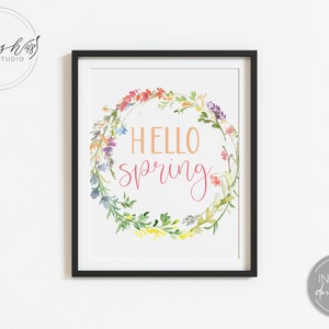 May include: A printable art print with a watercolor wreath of flowers in shades of pink, yellow, blue, and green. The wreath surrounds the text "Hello Spring" in pink and orange.