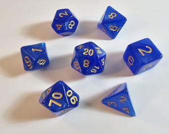 May include: Seven blue polyhedral dice with gold numbering are scattered on a white surface. The dice are various shapes, including a d20, d12, d10, d8, and d6. The dice have a shimmering, translucent appearance.