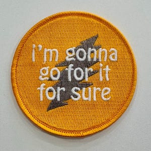 May include: Embroidered patch with the text "I'm gonna go for it for sure" in white lettering. The patch has a yellow background with a gray lightning bolt design. The patch is circular with a yellow border.