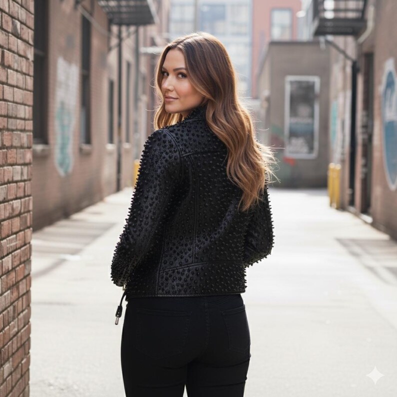 May include: A black jacket featuring a dense pattern of small, raised studs across the back and sleeves, paired with black pants. The jacket has a structured collar and a fitted silhouette, with a visible zipper pull detail at the lower side hem.